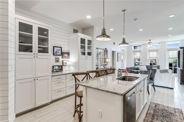 kitchen featuring white cabinets, a kitchen breakfast bar, open floor plan, a sink, and stainless steel dishwasher