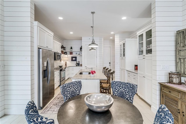 kitchen with stainless steel appliances, a sink, a center island with sink, white cabinets, and open shelves