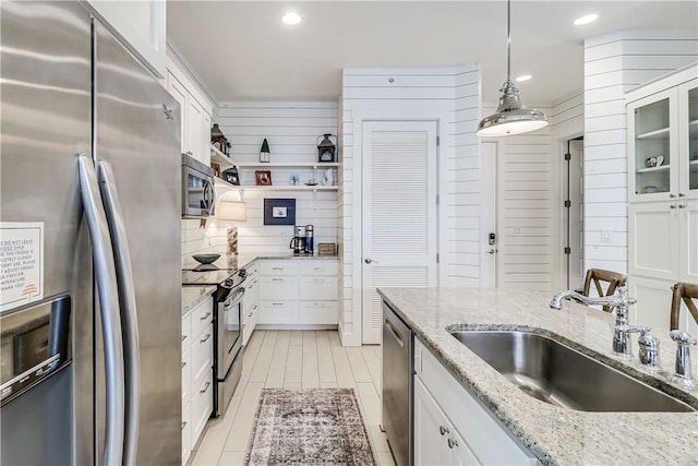 kitchen featuring appliances with stainless steel finishes, a sink, white cabinetry, decorative light fixtures, and glass insert cabinets