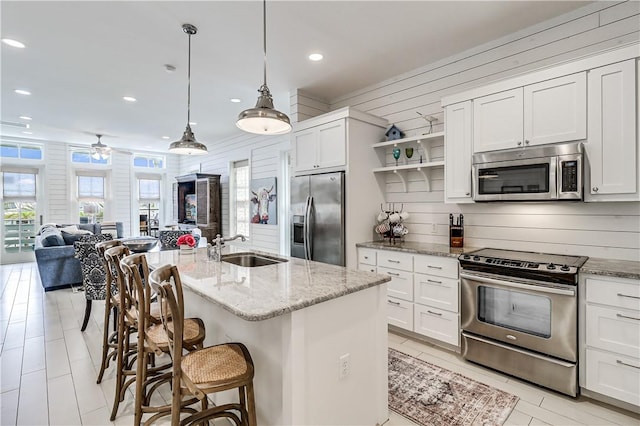 kitchen featuring light stone counters, stainless steel appliances, a sink, white cabinetry, and open shelves