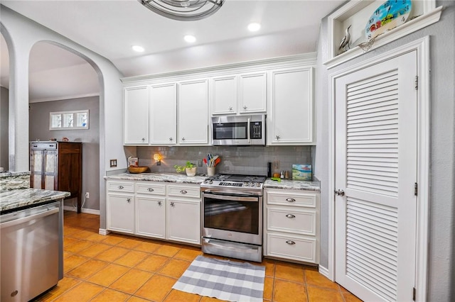 kitchen with light tile patterned floors, arched walkways, white cabinets, decorative backsplash, and stainless steel appliances