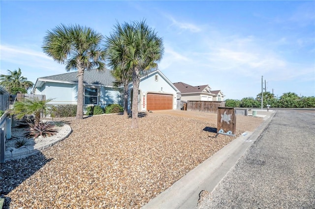 ranch-style home featuring an attached garage, driveway, fence, and stucco siding