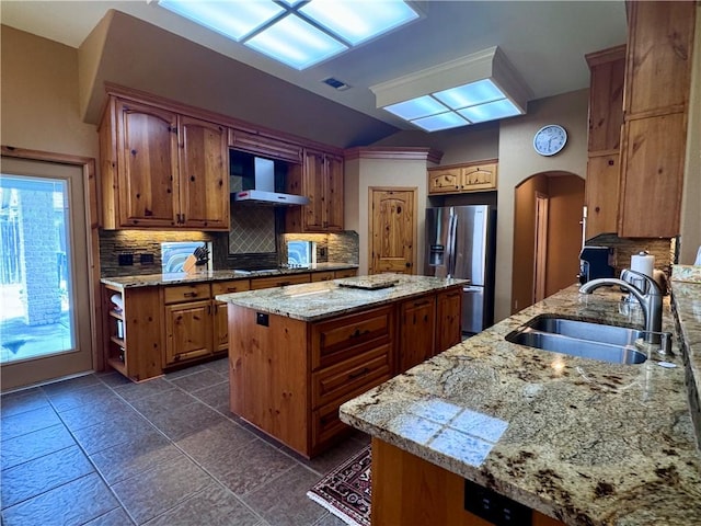 7605 Bayonne Dr, Corpus Christi, TX 78414 - kitchen featuring stainless steel fridge, wall chimney range hood, arched walkways, decorative backsplash, and a kitchen island