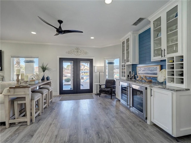 kitchen featuring wine cooler, light stone countertops, white cabinets, french doors, and light wood-type flooring