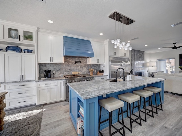 kitchen with premium range hood, a center island with sink, high quality appliances, light stone countertops, and white cabinets