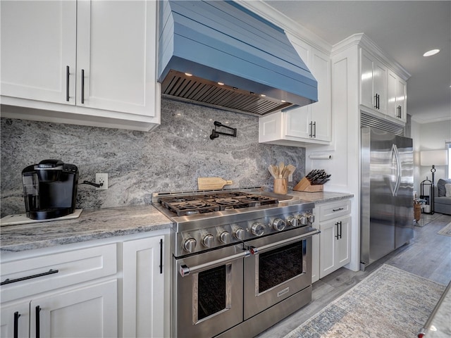 kitchen with extractor fan, tasteful backsplash, white cabinetry, premium appliances, and light stone counters