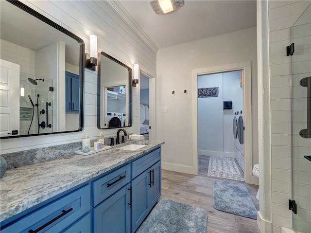 bathroom with washing machine and clothes dryer, toilet, a tile shower, vanity, and hardwood / wood-style floors