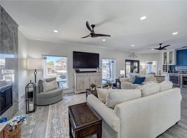 living room with crown molding, ceiling fan, a fireplace, and light wood-type flooring