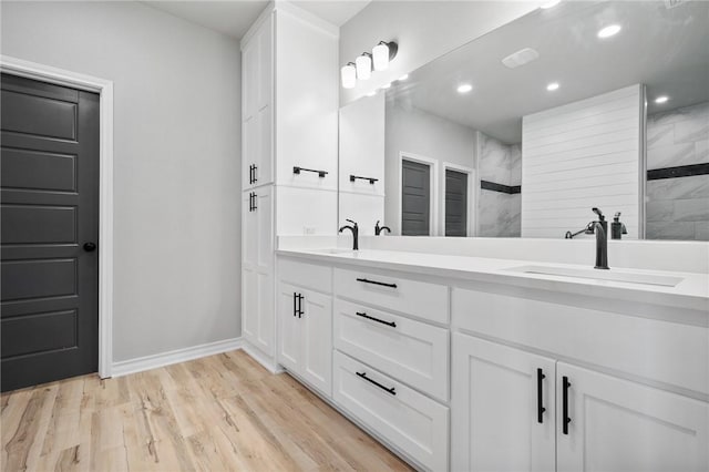 bathroom featuring double vanity, baseboards, wood finished floors, a sink, and recessed lighting