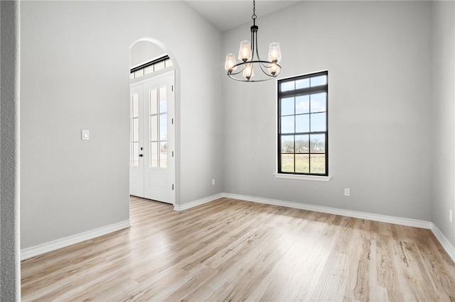 spare room featuring arched walkways, french doors, light wood finished floors, a chandelier, and baseboards