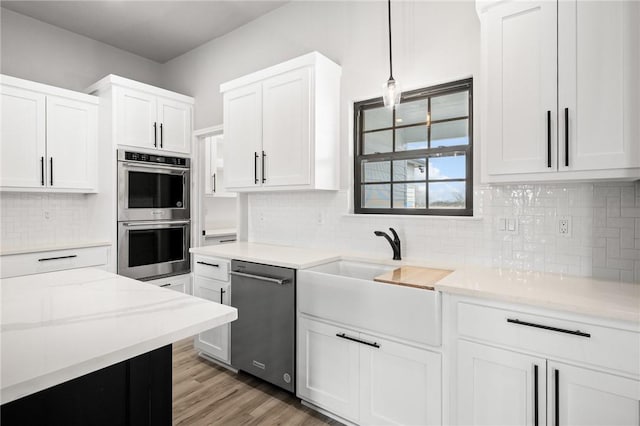 kitchen featuring white cabinetry, light wood-style floors, appliances with stainless steel finishes, decorative backsplash, and light stone countertops