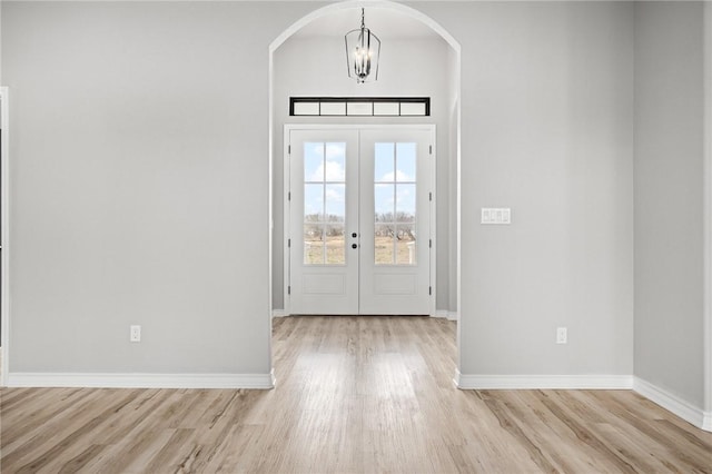 entryway with light wood-style flooring, baseboards, a chandelier, and arched walkways