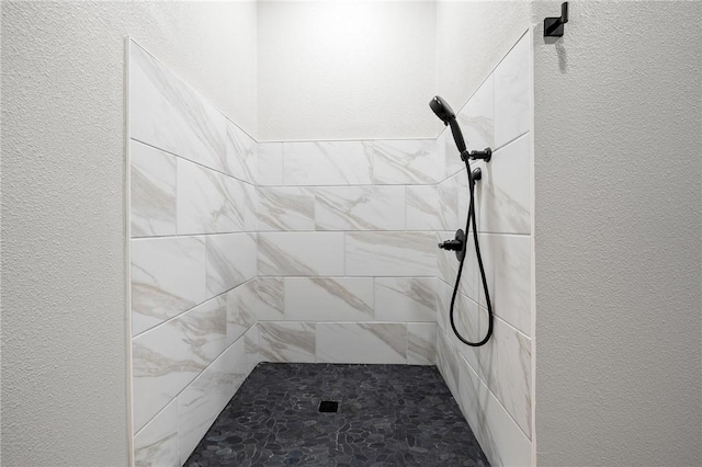 full bath featuring a tile shower and a textured wall