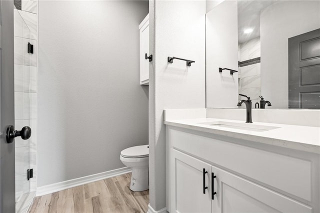 bathroom with toilet, wood finished floors, vanity, baseboards, and walk in shower