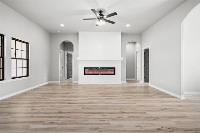 unfurnished living room featuring ceiling fan, recessed lighting, baseboards, light wood finished floors, and a glass covered fireplace