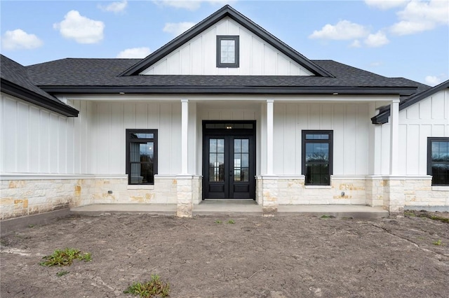 entrance to property featuring stone siding, a shingled roof, board and batten siding, and french doors