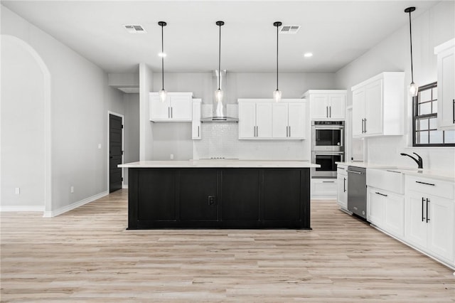 kitchen featuring wall chimney range hood, visible vents, appliances with stainless steel finishes, and a sink