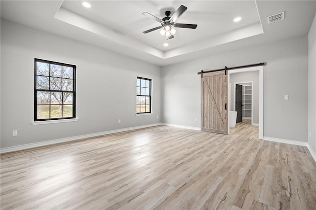 unfurnished bedroom with visible vents, multiple windows, a tray ceiling, and a barn door