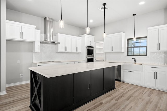 kitchen with wall chimney exhaust hood, stainless steel double oven, a kitchen island, and white cabinets