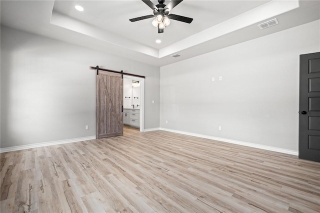 unfurnished room with a tray ceiling, visible vents, baseboards, and a barn door