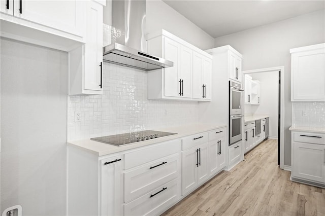 kitchen with black electric stovetop, light countertops, light wood-style floors, stainless steel double oven, and wall chimney range hood