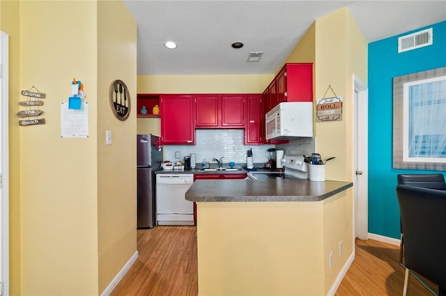 kitchen featuring white appliances, sink, backsplash, kitchen peninsula, and light hardwood / wood-style flooring