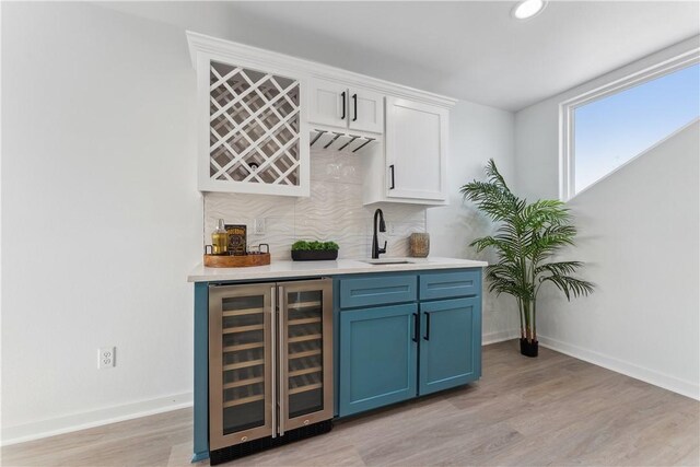 bar featuring decorative backsplash, a sink, indoor wet bar, light wood finished floors, and wine cooler