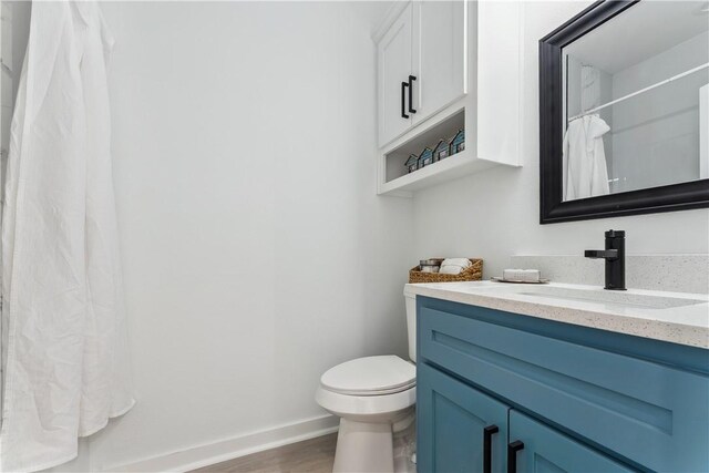 bathroom with baseboards, wood finished floors, toilet, and vanity