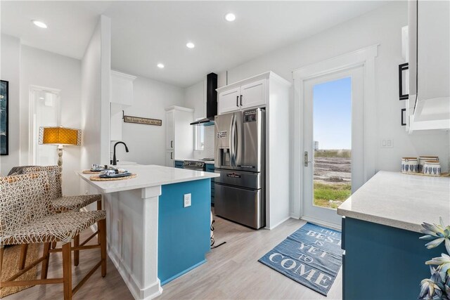 kitchen featuring stainless steel fridge, light wood-style flooring, wall chimney exhaust hood, and plenty of natural light