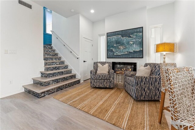 living room with a glass covered fireplace, recessed lighting, wood finished floors, visible vents, and stairway