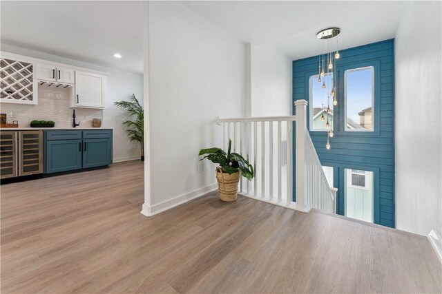 interior space with bar, baseboards, beverage cooler, recessed lighting, and light wood-style flooring