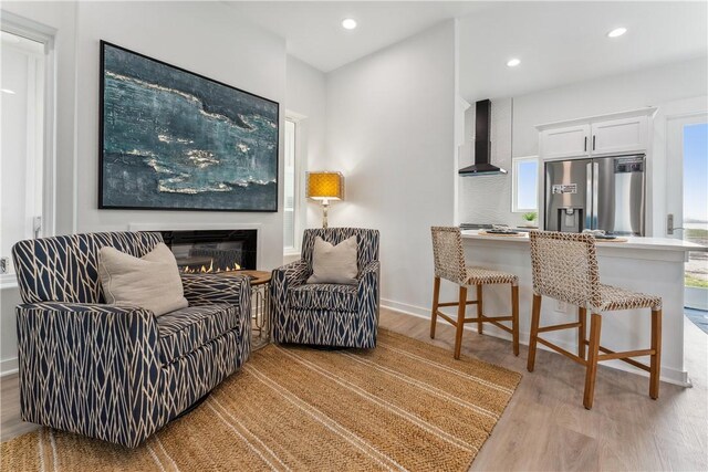 living area with recessed lighting, baseboards, a glass covered fireplace, and light wood-type flooring