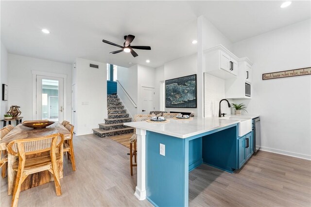 kitchen with a sink, light wood-style floors, a ceiling fan, and blue cabinetry