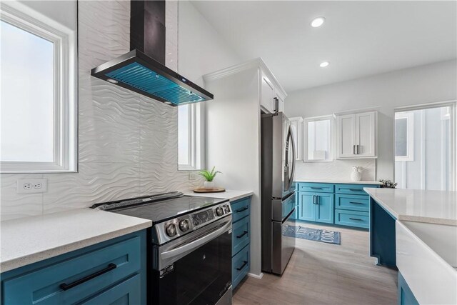 kitchen featuring white cabinets, wall chimney exhaust hood, stainless steel appliances, decorative backsplash, and blue cabinets