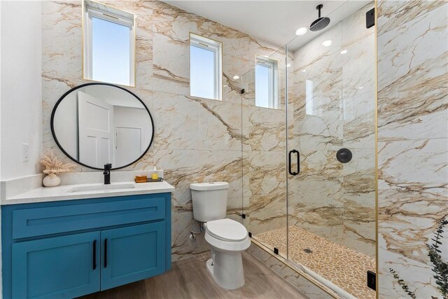 bathroom with vanity, toilet, a marble finish shower, tile walls, and wood finished floors