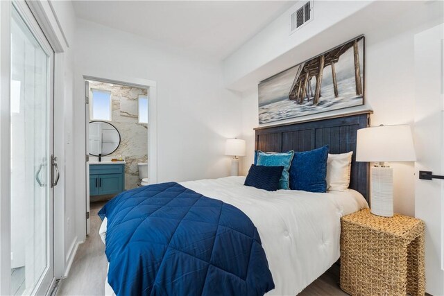 bedroom featuring ensuite bathroom, wood finished floors, and visible vents
