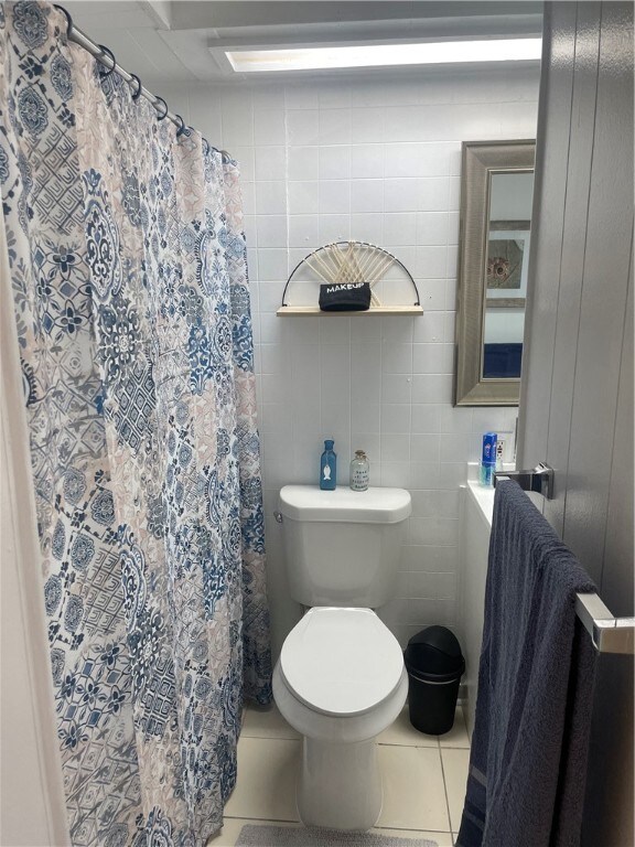 bathroom with tile walls, tile patterned flooring, a shower with shower curtain, and toilet