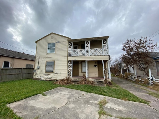 view of property with covered porch, a balcony, and a front yard