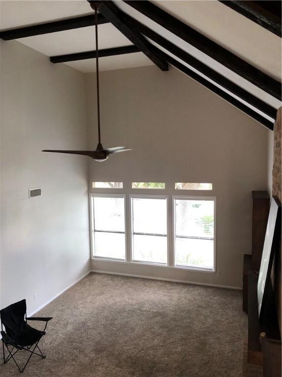 unfurnished living room with ceiling fan, high vaulted ceiling, beam ceiling, and carpet floors