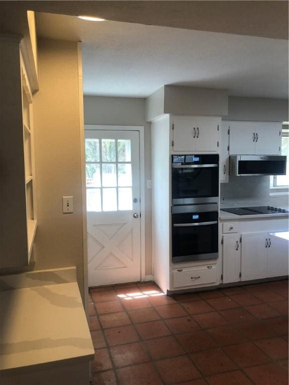 kitchen with multiple ovens, ventilation hood, white cabinets, dark tile patterned floors, and black electric stovetop