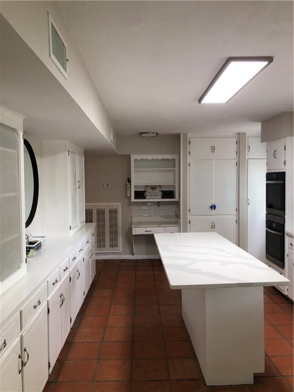 kitchen with black double oven, a center island, dark tile patterned flooring, and white cabinets