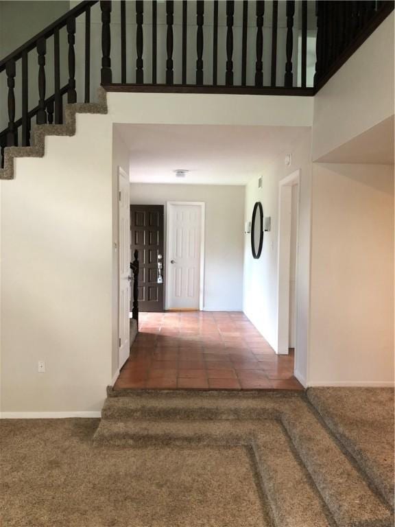 hallway with a towering ceiling and dark colored carpet