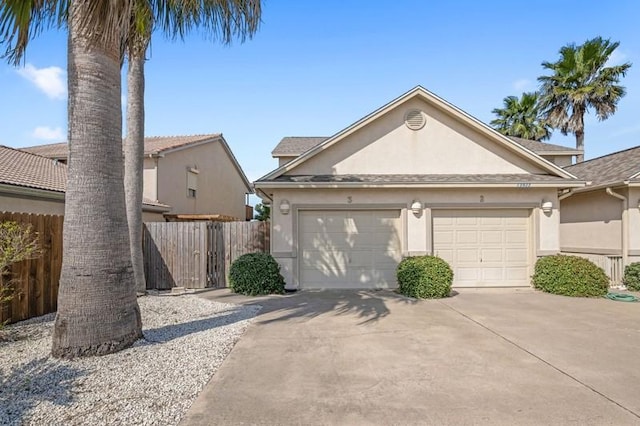 view of front facade featuring concrete driveway, fence, an attached garage, and stucco siding