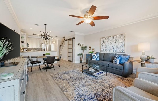 living room featuring a barn door, light wood-style flooring, ceiling fan with notable chandelier, visible vents, and crown molding