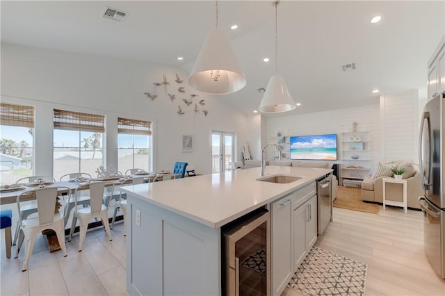 kitchen featuring pendant lighting, sink, beverage cooler, a kitchen island with sink, and stainless steel appliances