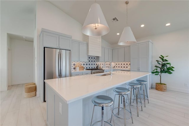 kitchen with sink, tasteful backsplash, decorative light fixtures, a large island with sink, and stainless steel fridge