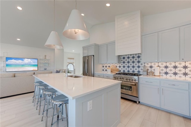 kitchen featuring pendant lighting, tasteful backsplash, an island with sink, sink, and stainless steel appliances