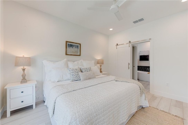 bedroom with ceiling fan, a barn door, and light hardwood / wood-style floors