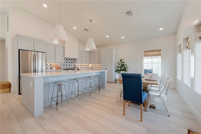 kitchen featuring a breakfast bar area, tasteful backsplash, hanging light fixtures, a center island with sink, and stainless steel fridge