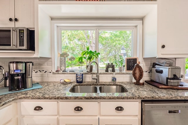 kitchen with light stone countertops, appliances with stainless steel finishes, backsplash, sink, and white cabinets